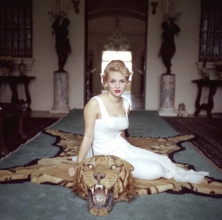 slim-aarons-lady-daphne-cameron-mrs-george-cameron-on-a-tiger-skin-rug-in-the-trophy-room-at-socialite-laddie-sanfords-home-in-palm-beach-florida-1959